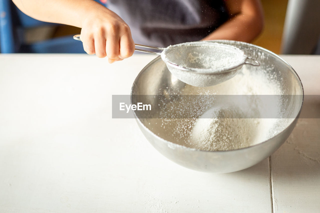 A close view of the hand of the child sifting flour