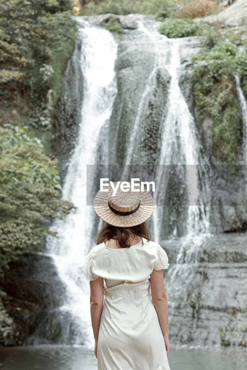 Rear view of woman standing against waterfall