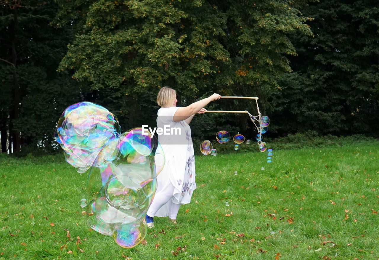 Smiling woman making bubbles while standing against trees