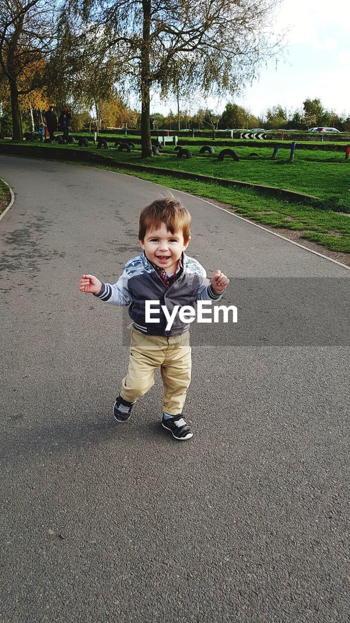 Portrait of smiling boy standing on footpath in park