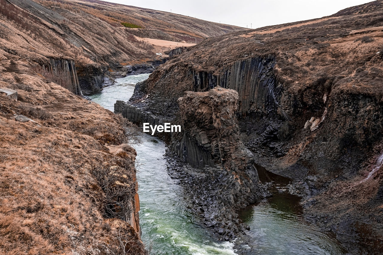 Stream flowing amidst basalt columns rock formation at eastfjords against sky