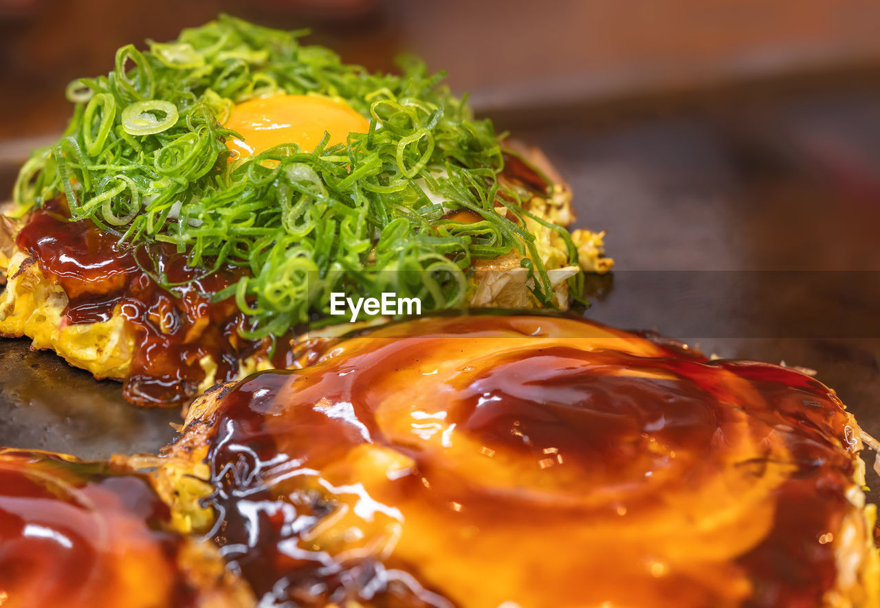 Close-up on a fried egg topped with great deal of chopped scallions on an okonomiyaki omelet