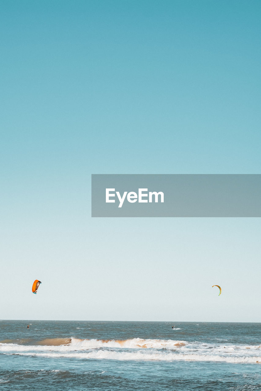 Scenic view of kitesurfers on sea against clear sky