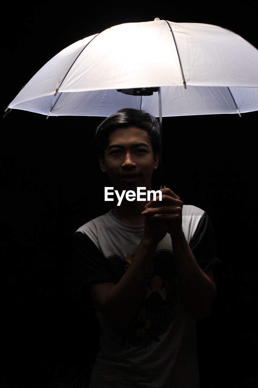 Man holding umbrella against black background