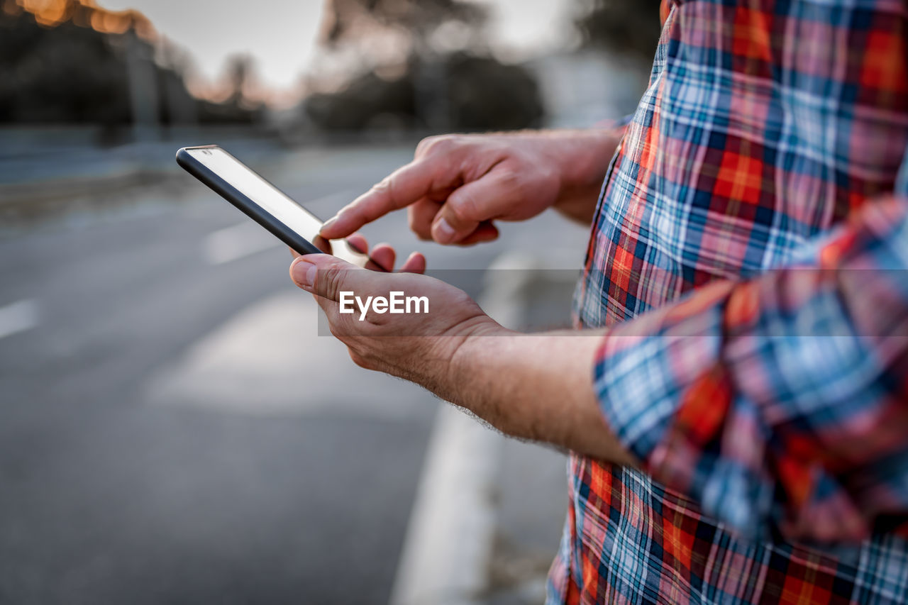 Close-up view of businessman  walking in the street and typing messages on his mobile phone. 