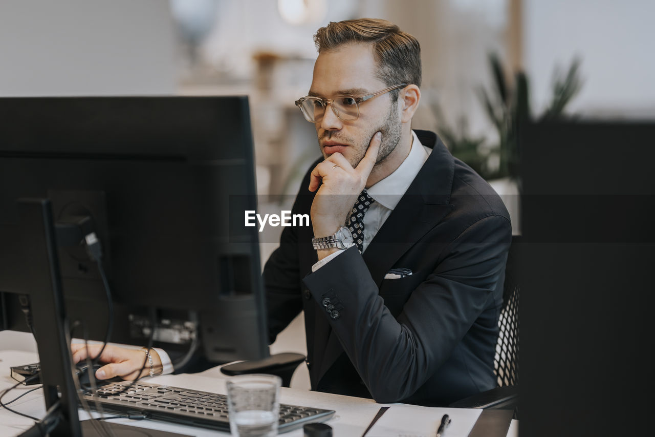 Confident young businessman using computer at desk in office