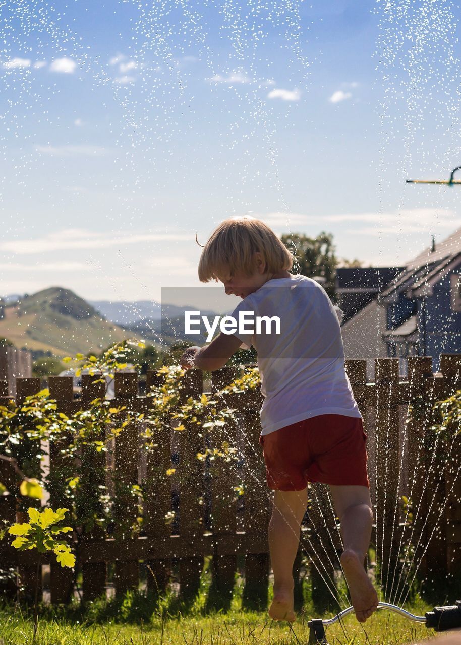 Rear view of boy running through water sprinkler