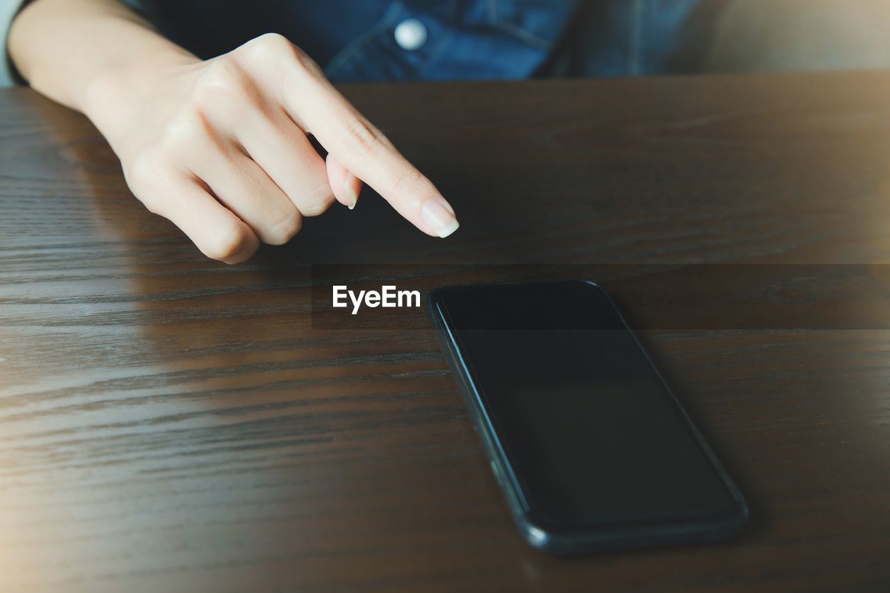 Cropped hand of woman by mobile phone on table