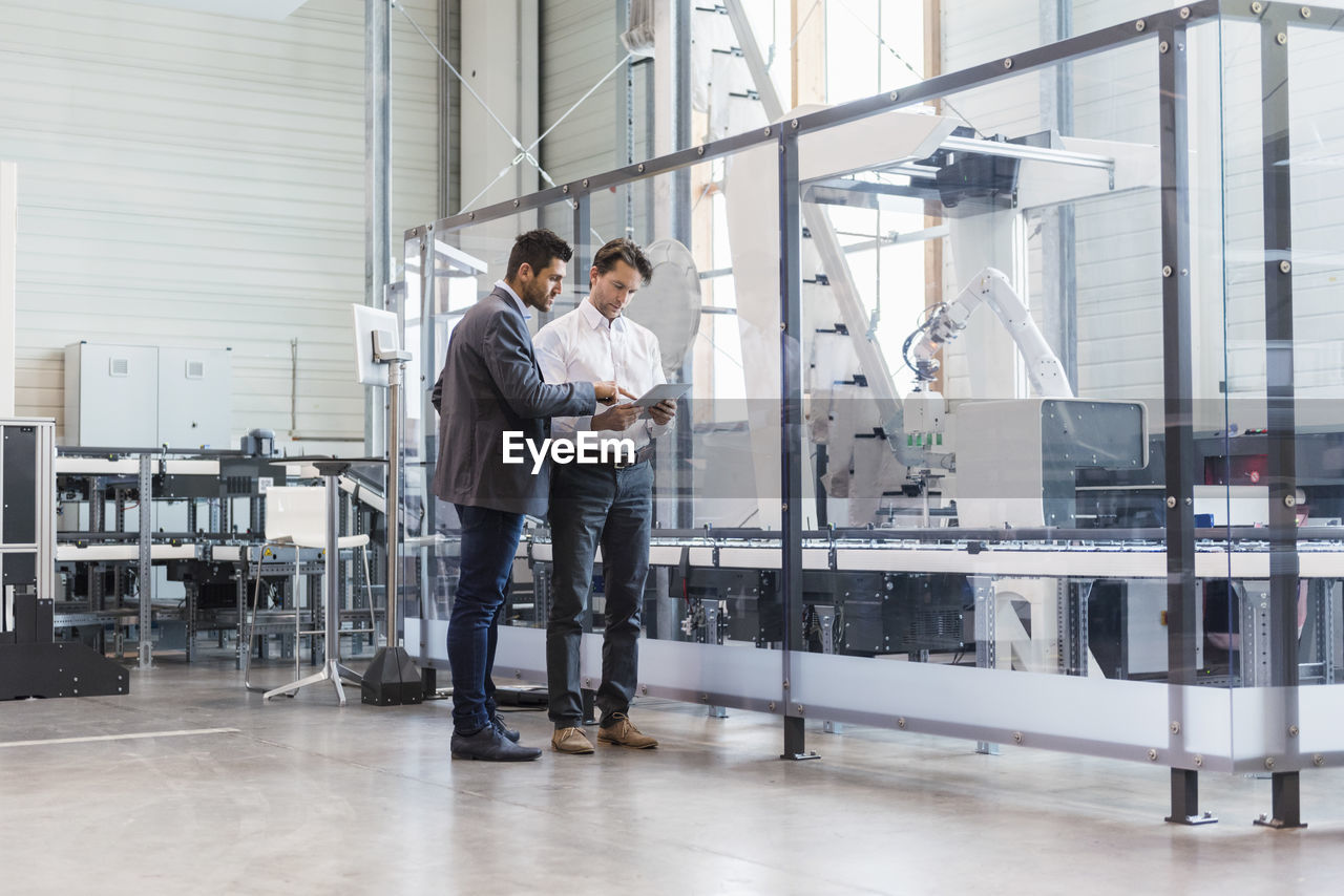 Two businessmen with tablet talking in modern factory