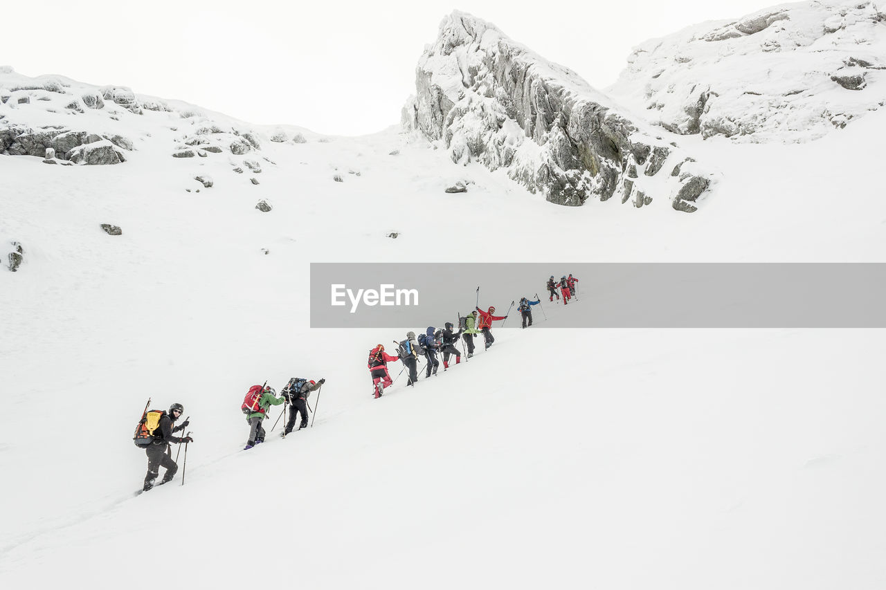 Low angle view of hikers climbing snow covered mountain