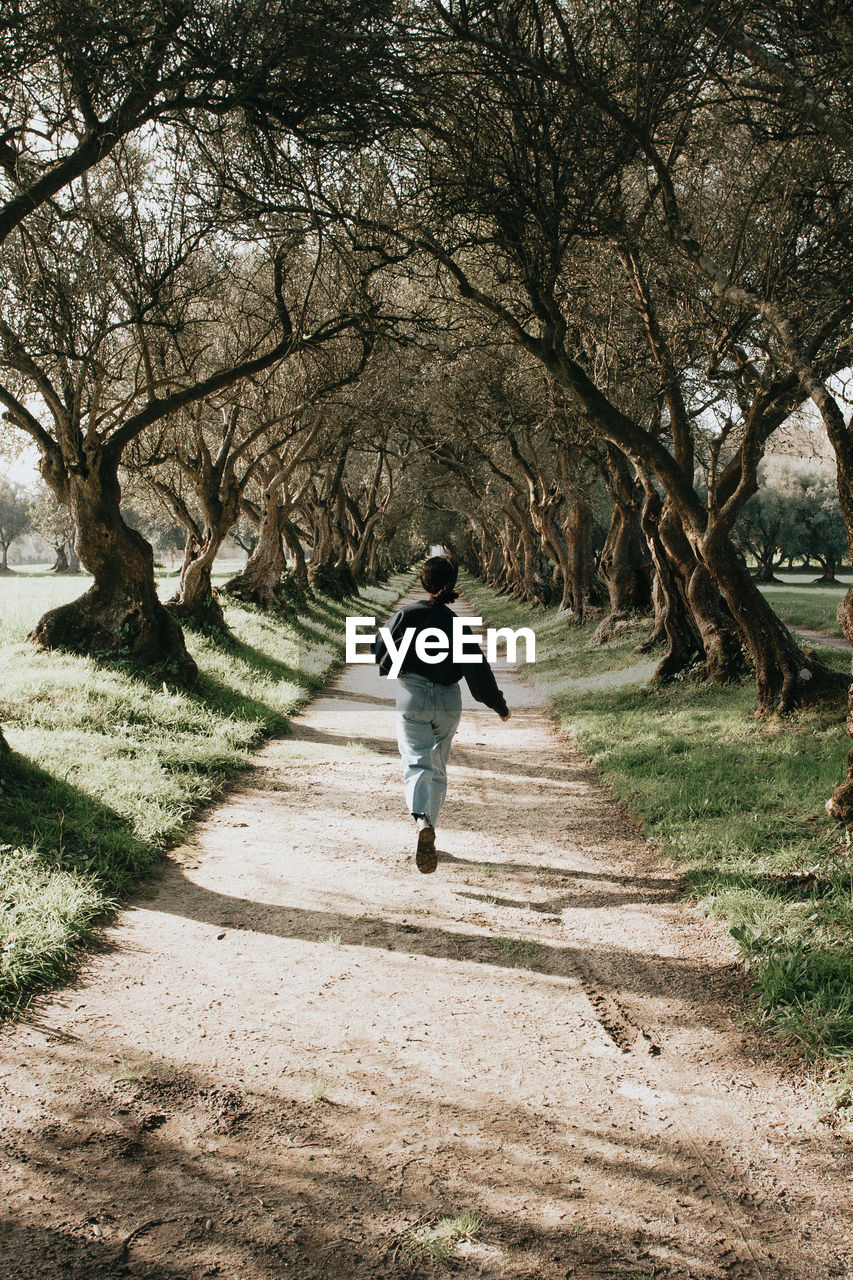 REAR VIEW OF MAN WALKING ON FOOTPATH AMIDST TREES