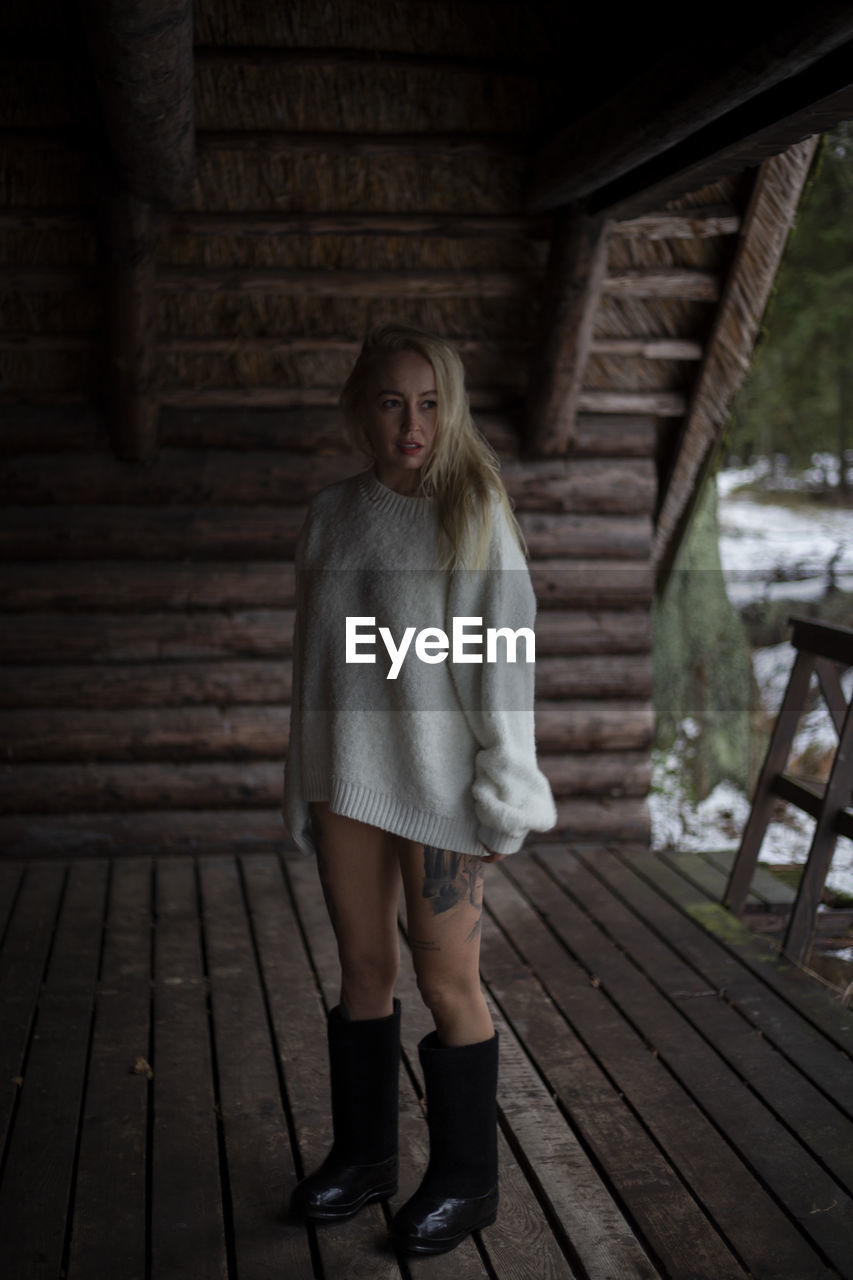 one person, full length, wood, adult, women, clothing, standing, architecture, portrait, footwear, young adult, blond hair, emotion, front view, looking at camera, dress, fashion, hairstyle, casual clothing, female, built structure, fear, lifestyles, long hair, photo shoot, spooky, shoe, darkness, day, outdoors