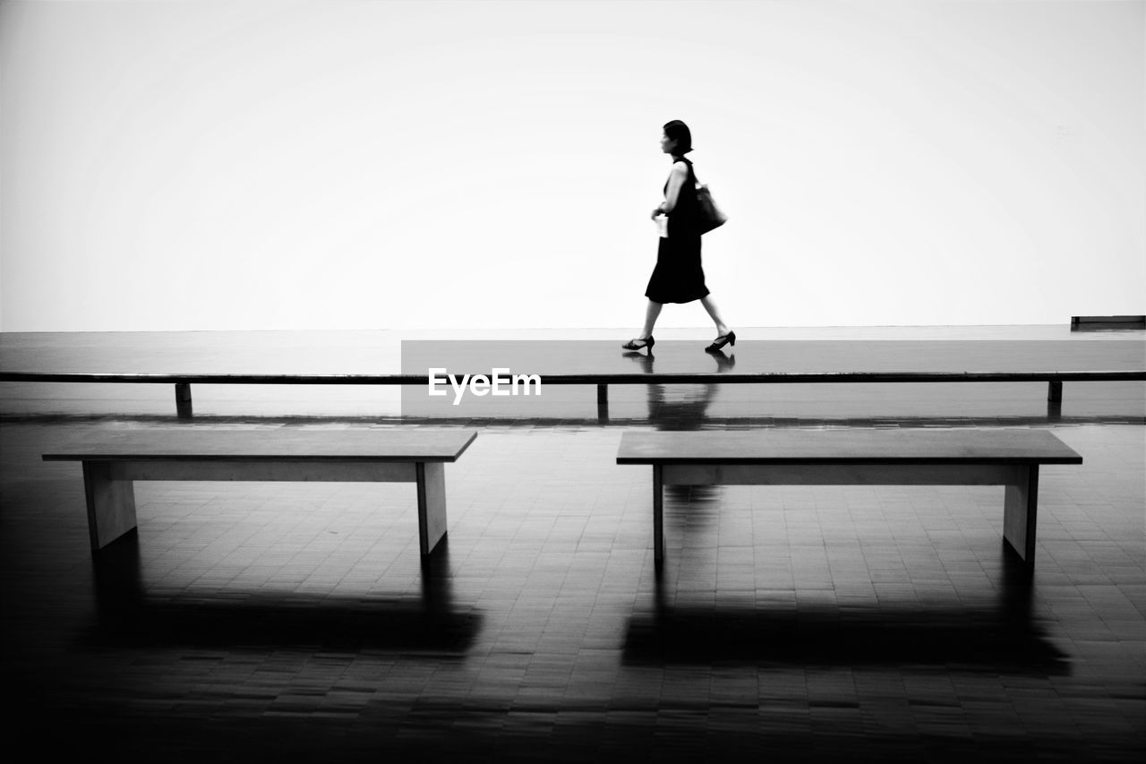 Full length of woman walking on footpath by benches during monsoon