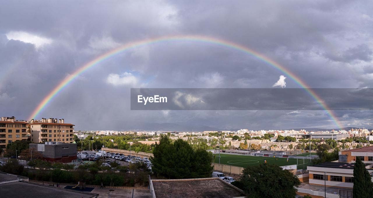 rainbow over cityscape against cloudy sky