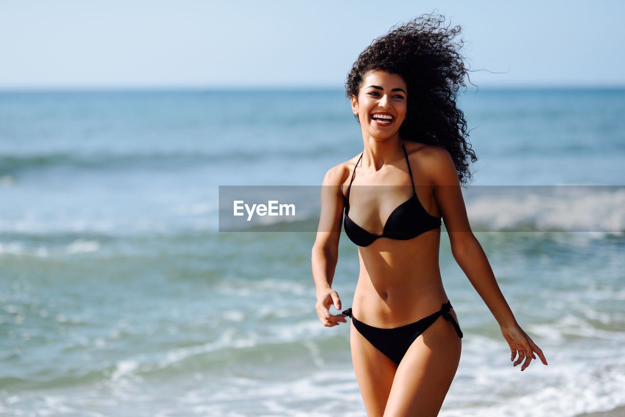 Cheerful young woman wearing black bikini at beach