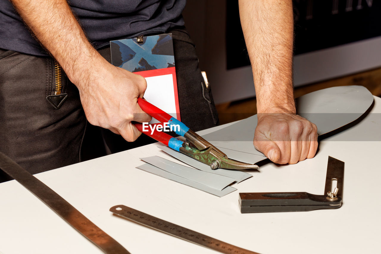 A worker cuts a sheet of roofing iron with metal scissors.