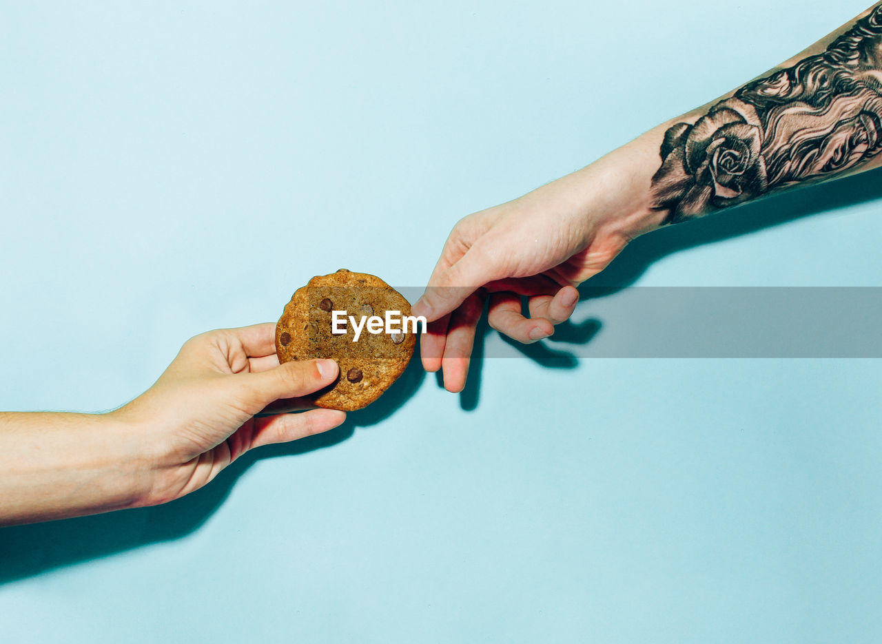 Cropped hands holding cookies against blue background