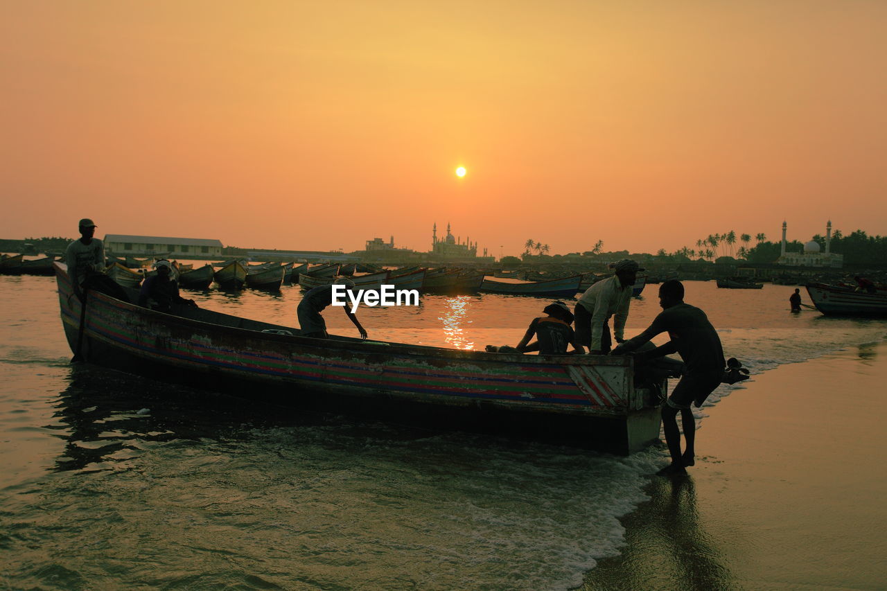 Men pulling out fishing boat in sea at sunset