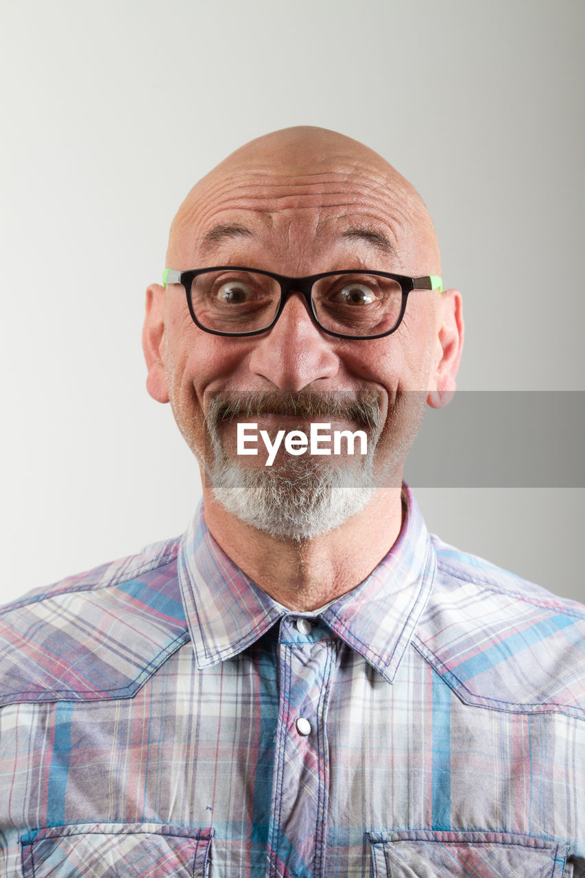 Close-up portrait of happy mature man making face against gray background