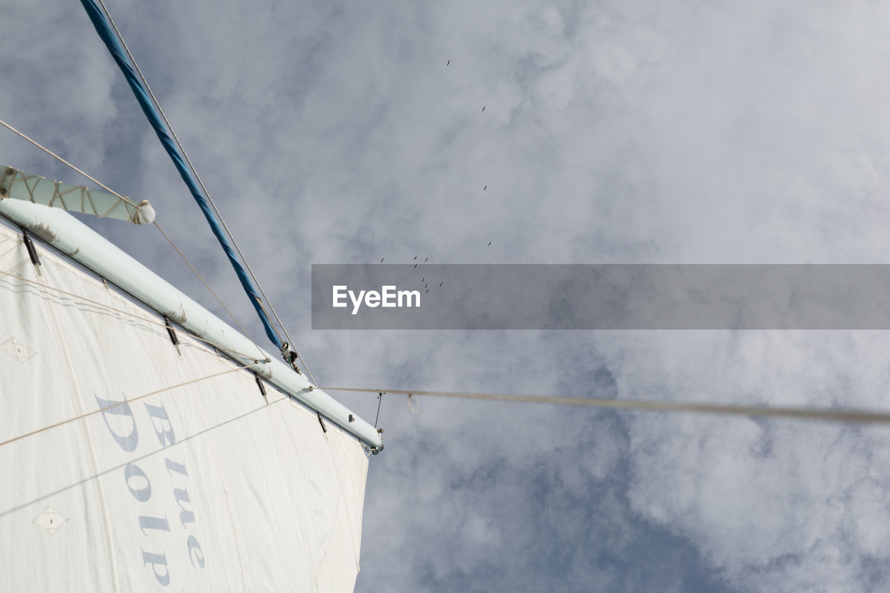 Sail and mast under sky with clouds