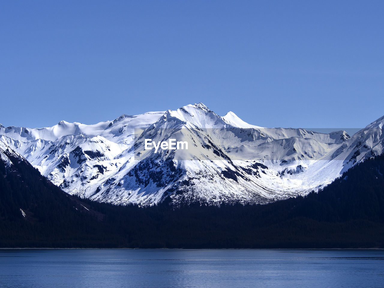 Idyllic shot of snowcapped mountain by river against clear blue sky