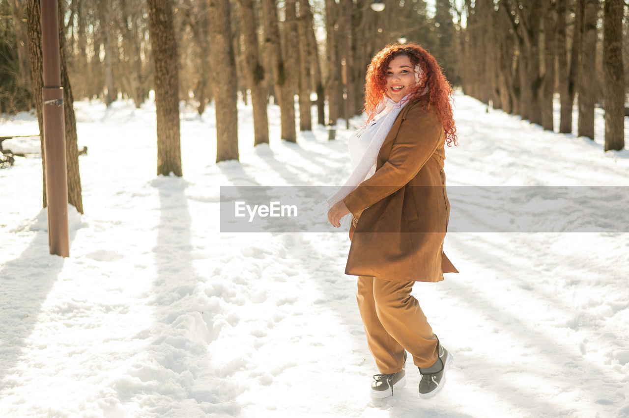 portrait of smiling young woman standing on snow covered land