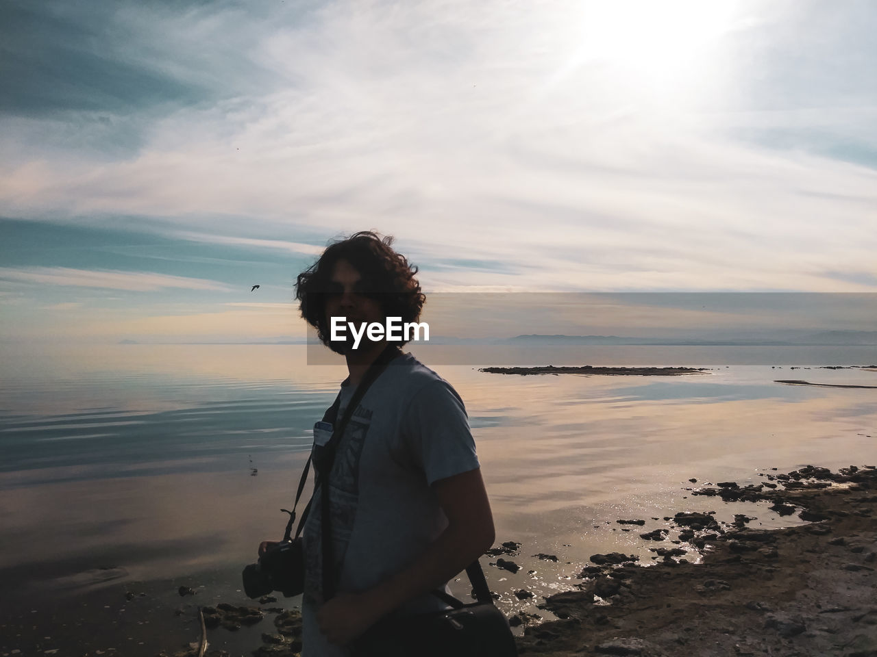 MAN STANDING ON SHORE AGAINST SKY DURING SUNSET