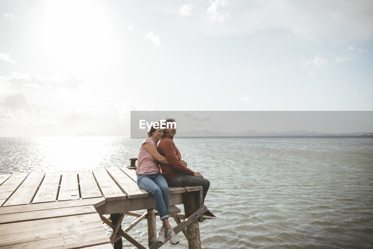 Mature couple sitting on jetty over sea