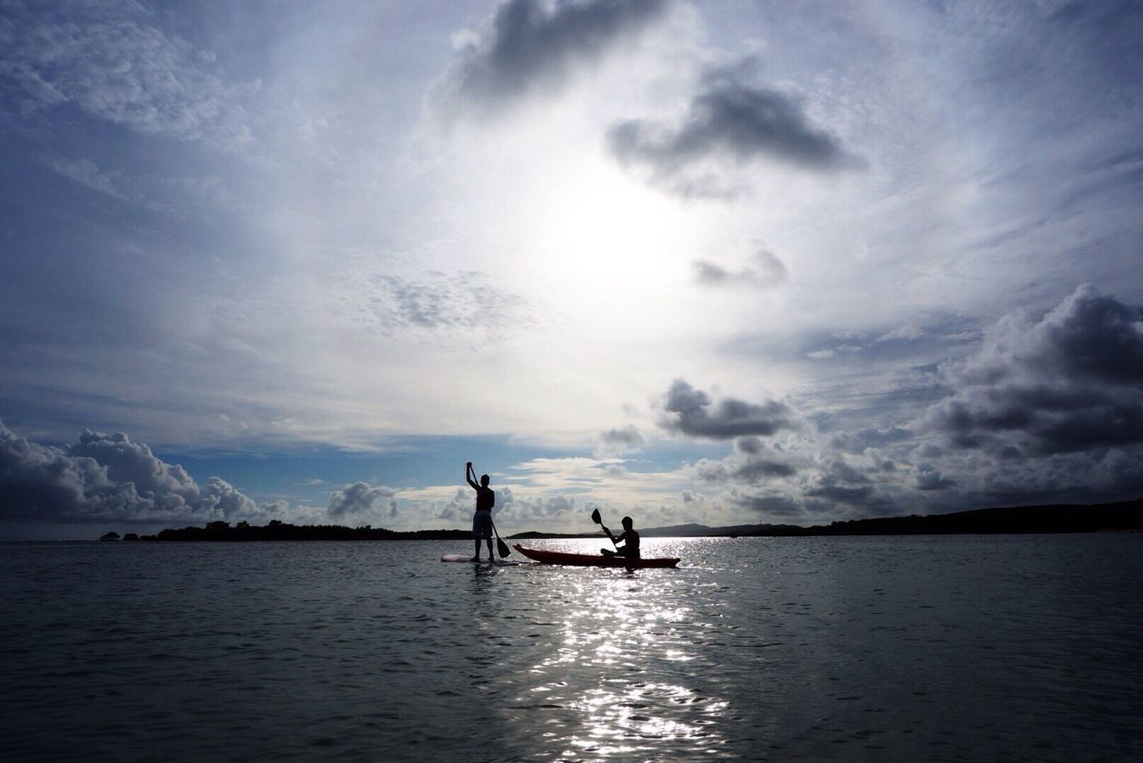 Man in boat by friend paddleboarding on sea against sky