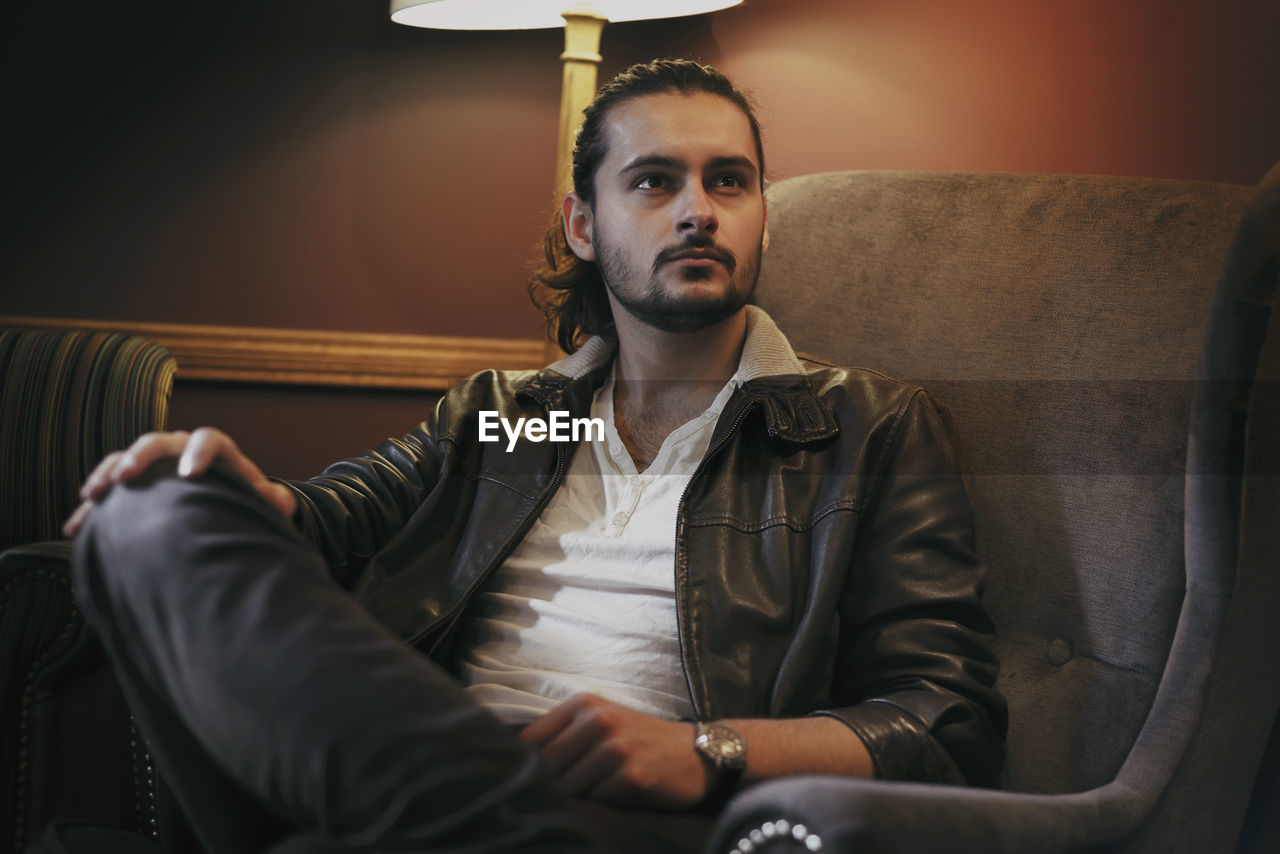 Thoughtful young man sitting on armchair at home