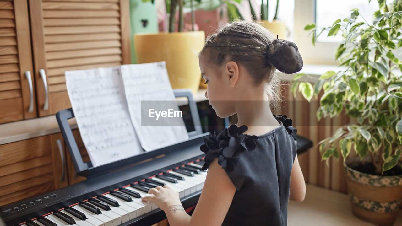 Rear view of girl playing piano at home