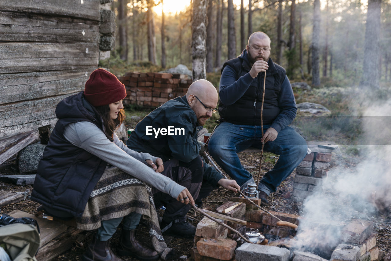 People preparing sausages over log fire
