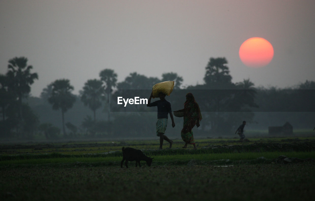 Farmers walking on field against sky