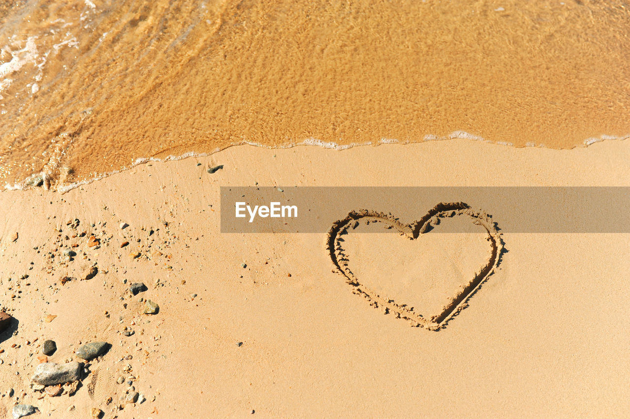 Painted heart on clean sand of beach and a wave of clear transparent water rolls, not glossy image