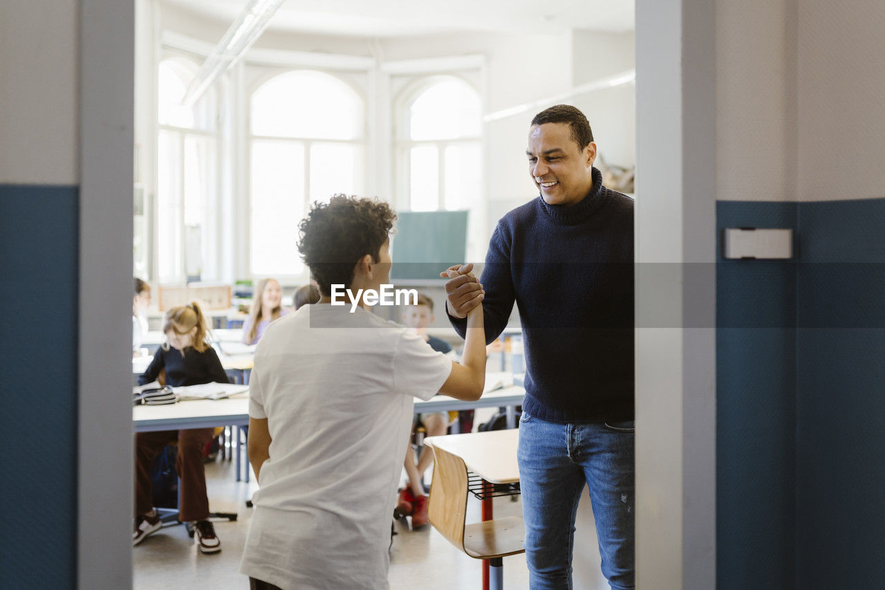 Smiling male teacher doing handshake with student in classroom