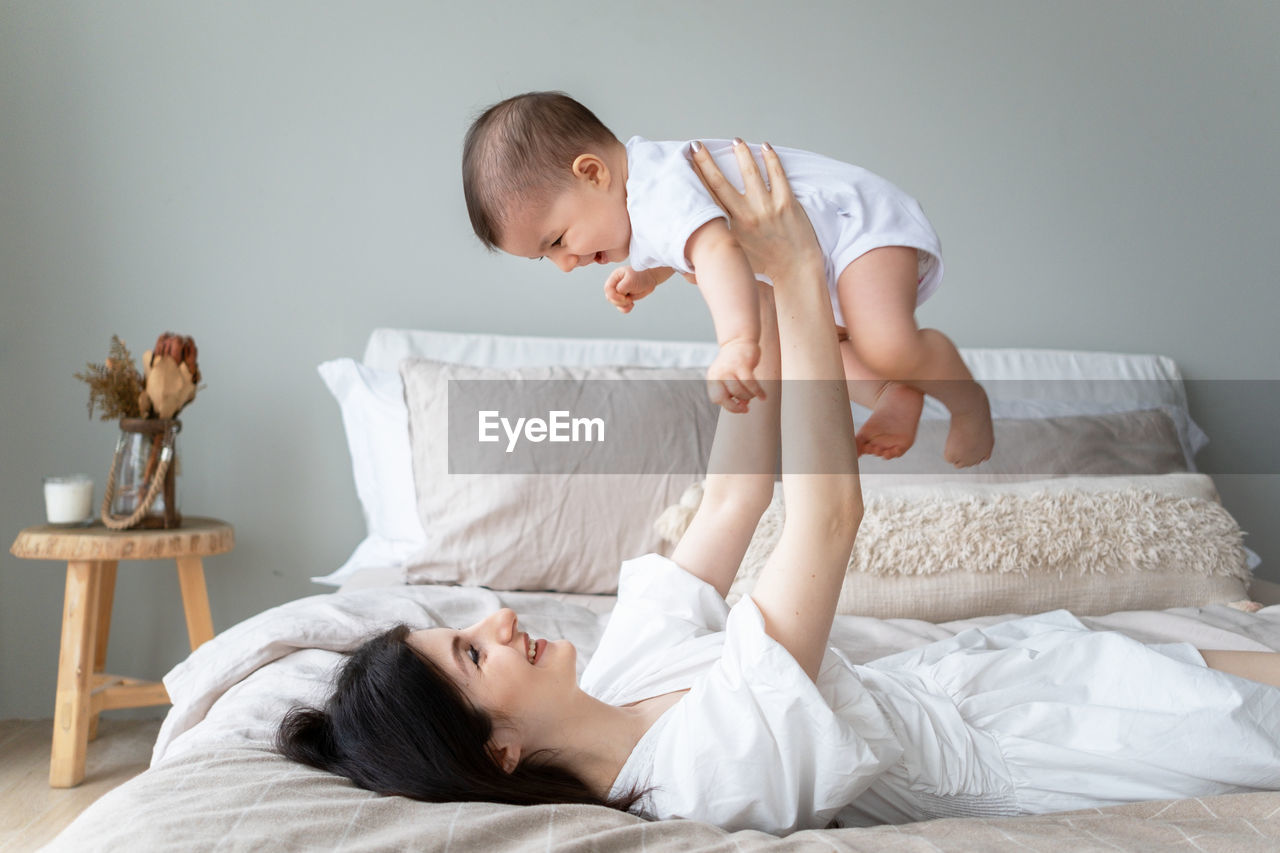 Smiling mother playing with baby on bed at home