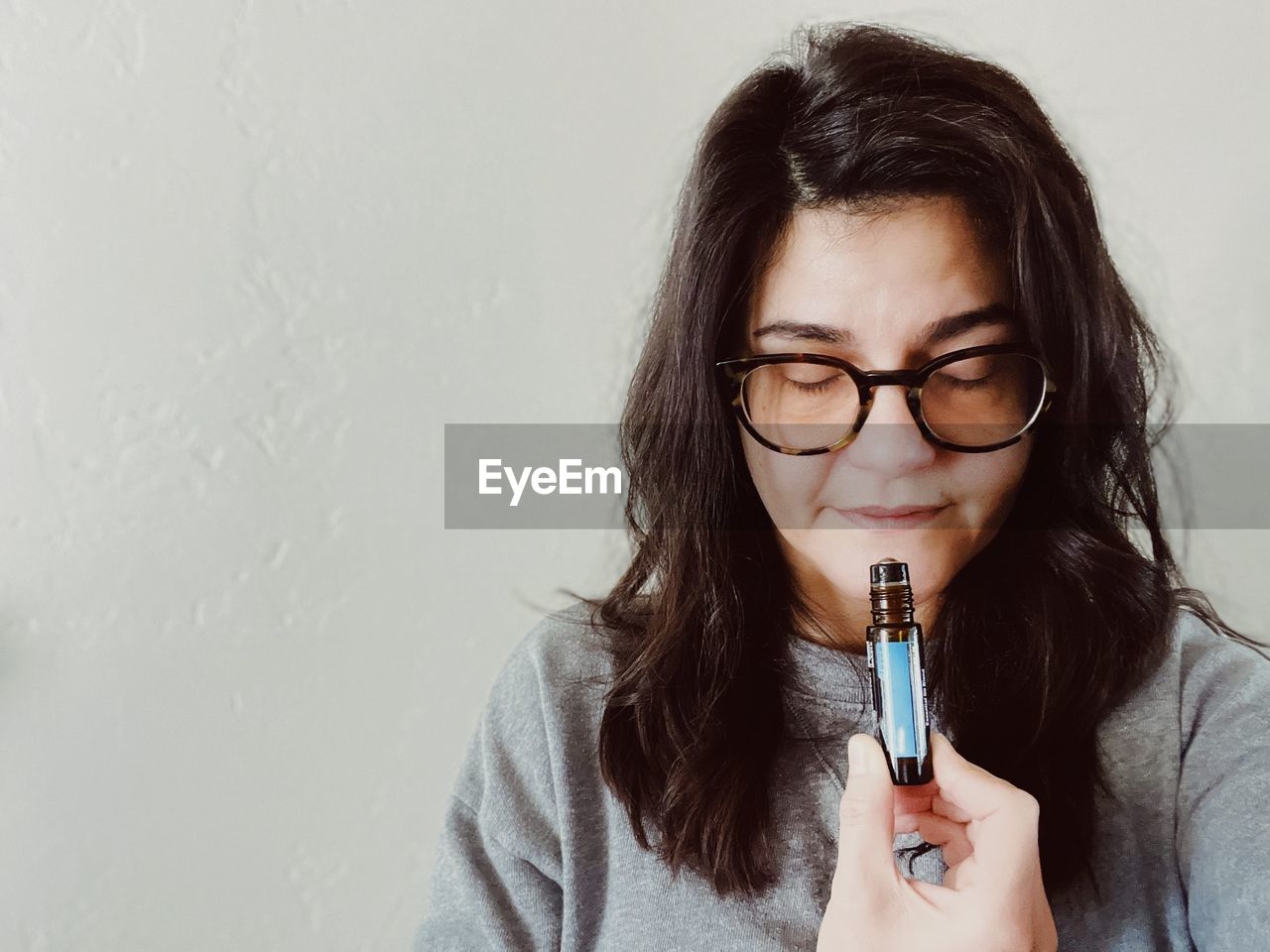 Portrait of young woman applying make-up and perfume  against wall