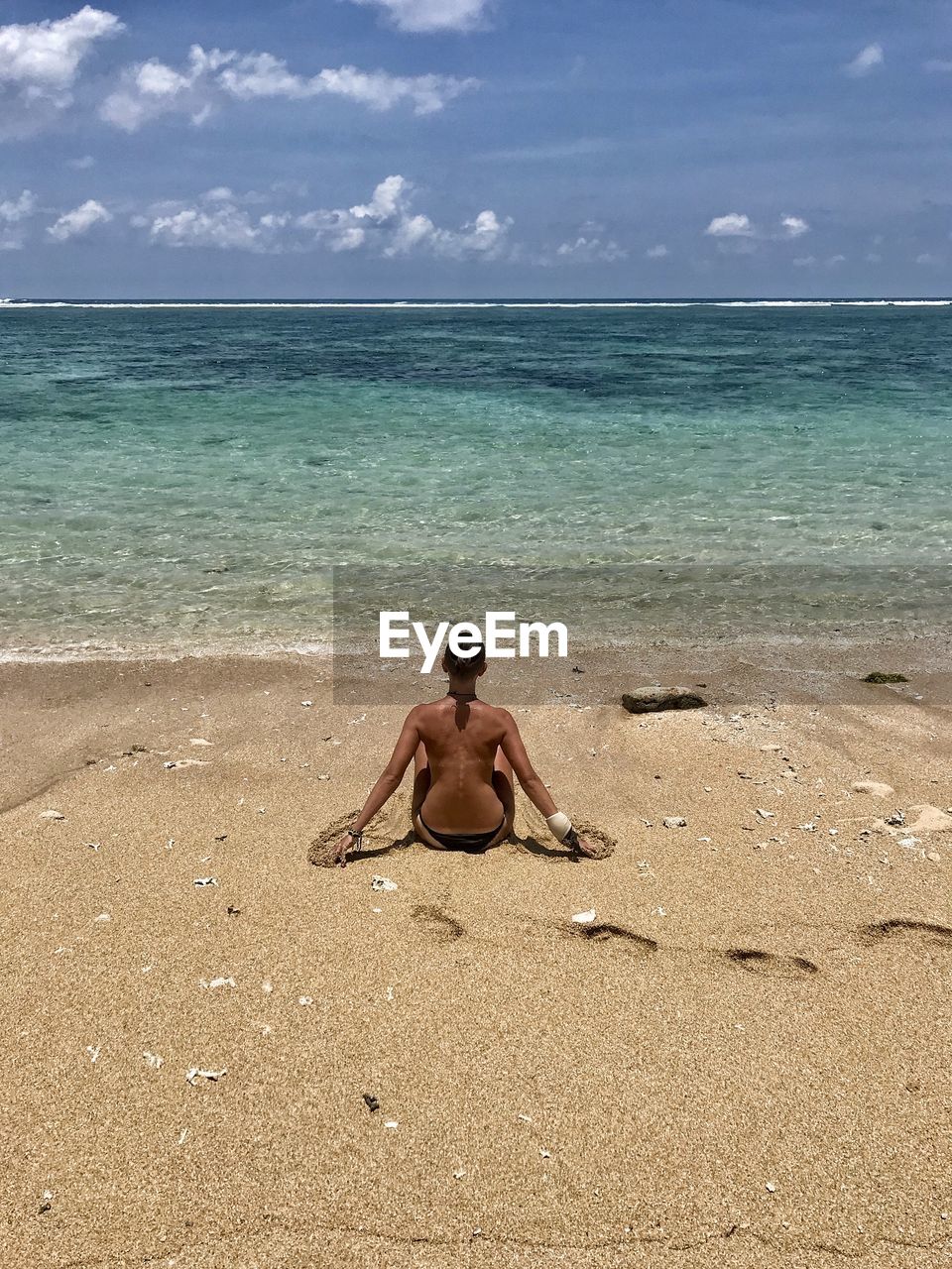 Full length of shirtless woman on beach against sky