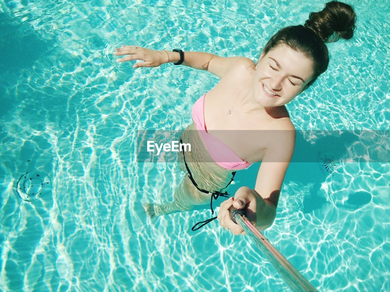 High angle view of woman wearing bikini taking selfie from monopod in swimming pool on sunny day