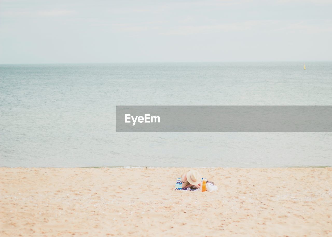 Woman relaxing on beach against sky