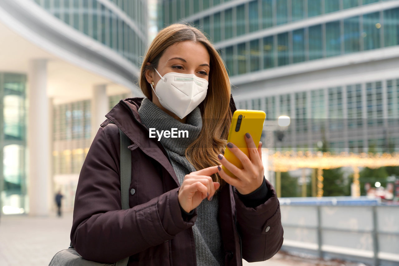 Woman with winter clothes typing finger chatting with someone on smartphone wearing protective mask