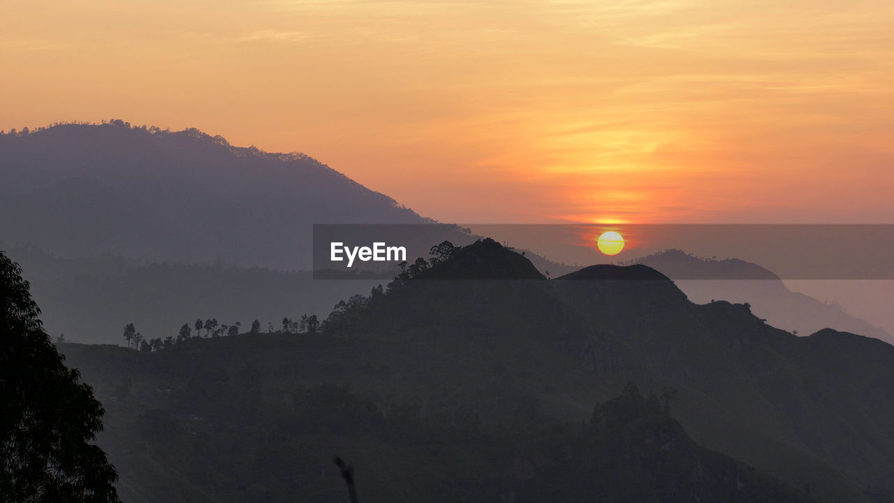 Scenic view of silhouette mountains against orange sky