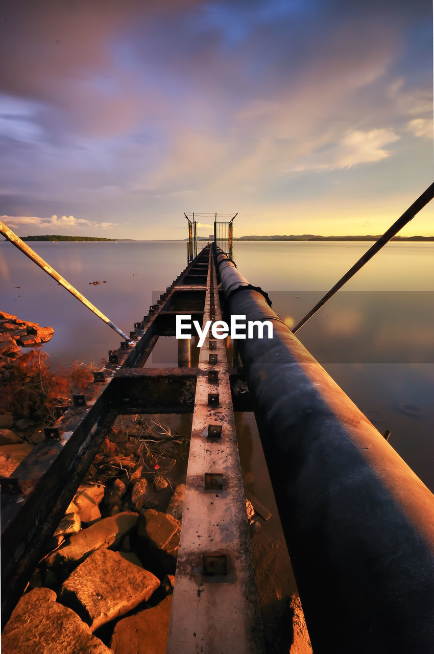 Pipeline over river against sky during sunset