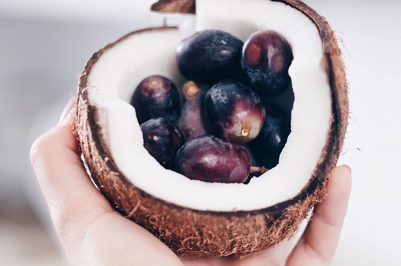 Cropped image of hand holding coconut and fruits