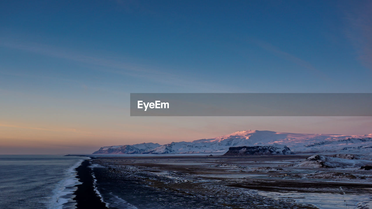 Scenic view of sea by snowcapped mountains against sky during sunset