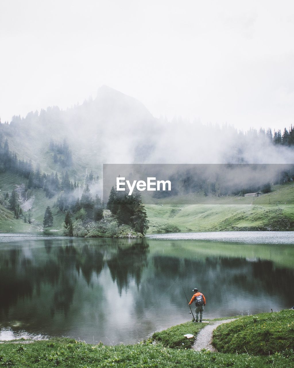 Man holding fishing rod while standing by lake against sky