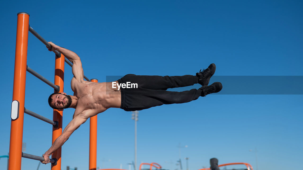 low angle view of man exercising against blue sky