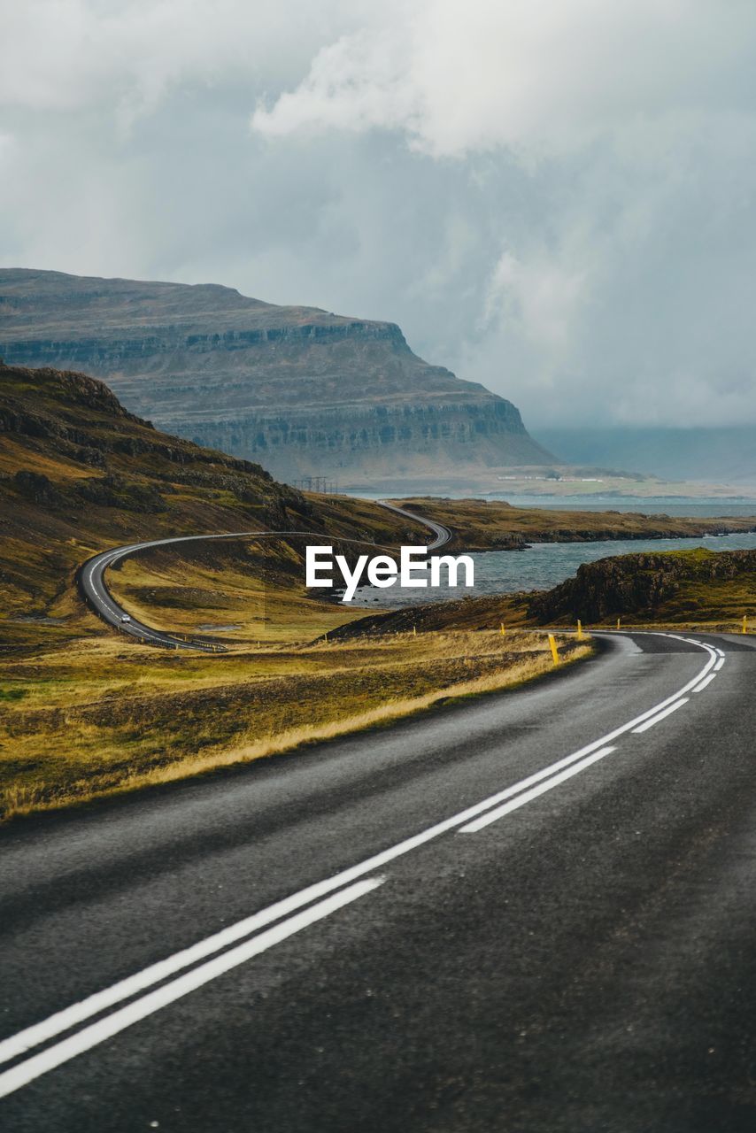 Empty road amidst landscape against cloudy sky