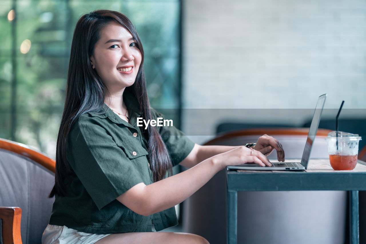 portrait of young woman using mobile phone while sitting on chair at home