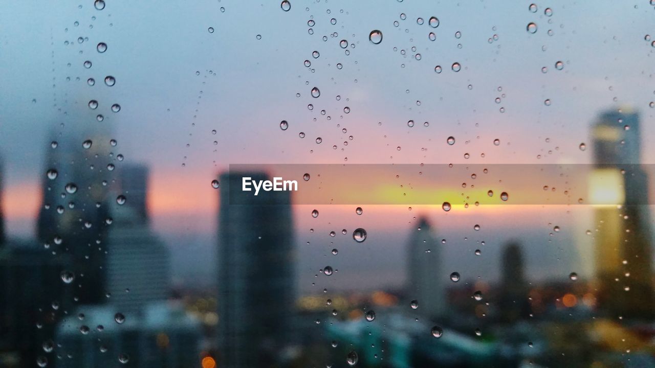 Cityscape seen through wet window during sunset